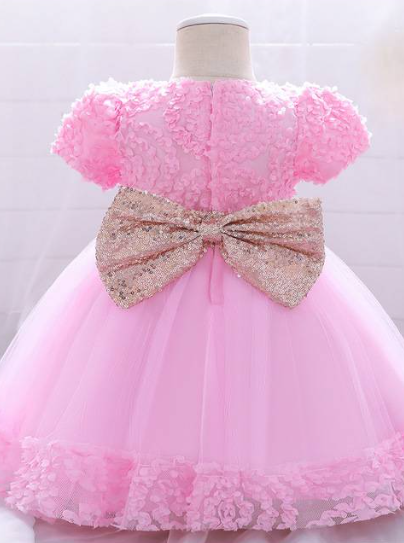 Baby dress has a floral bodice, a tulle skirt with floral hem, and a gold sequin belt with bow at the front and back