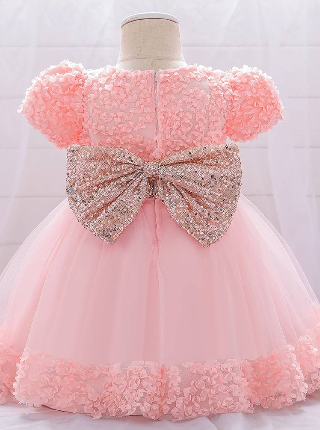 Baby dress has a floral bodice, a tulle skirt with floral hem, and a gold sequin belt with bow at the front and back