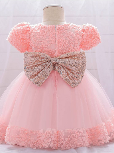Baby dress has a floral bodice, a tulle skirt with floral hem, and a gold sequin belt with bow at the front and back