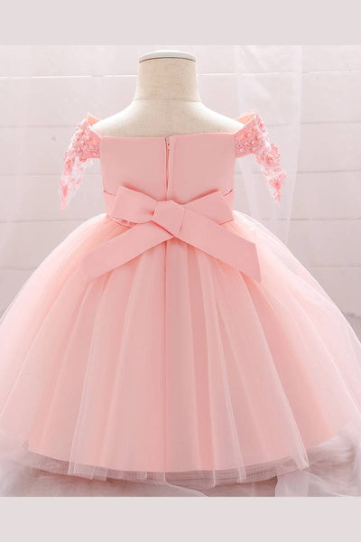 Baby dress has a satin embroidered bodice with pearl details and capped sleeves, a bow belt at the waist, and a tulle skirt with flower applique