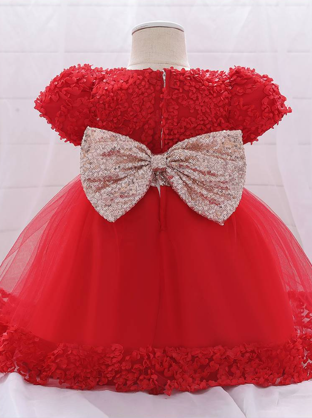 Baby dress has a floral bodice, a tulle skirt with floral hem, and a gold sequin belt with bow at the front and back