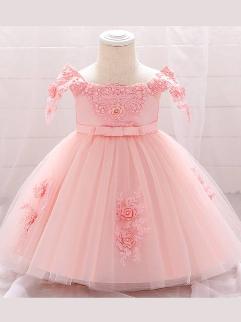 Baby dress has a satin embroidered bodice with pearl details and capped sleeves, a bow belt at the waist, and a tulle skirt with flower applique