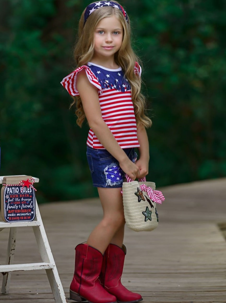 Girls 4th of July set features an American flag print flutter sleeve top with fringe neckline and patched denim shorts with a sash