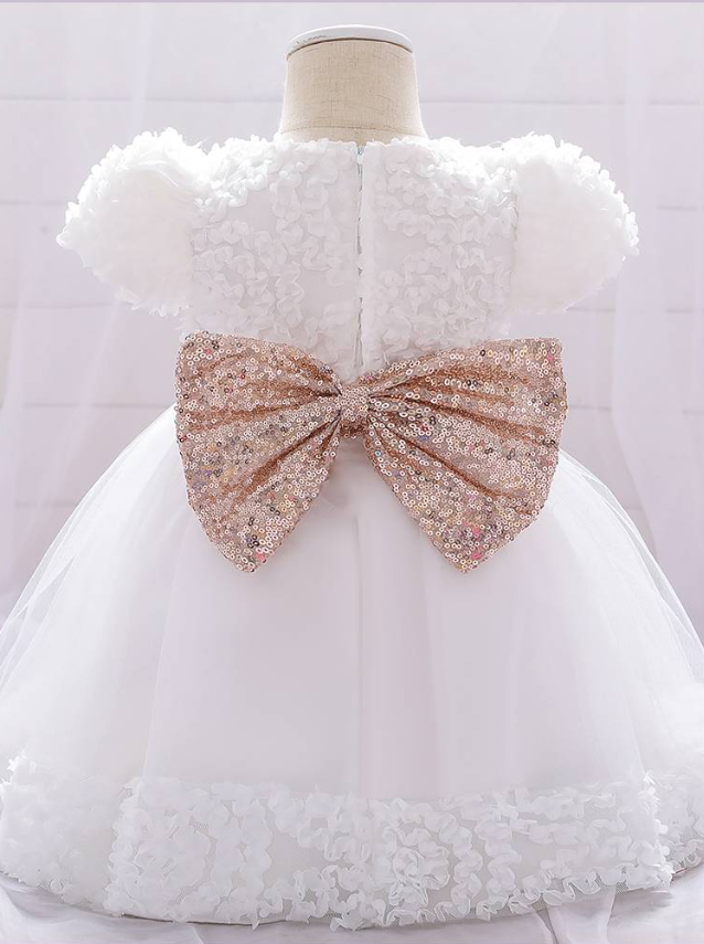 Baby dress has a floral bodice, a tulle skirt with floral hem, and a gold sequin belt with bow at the front and back