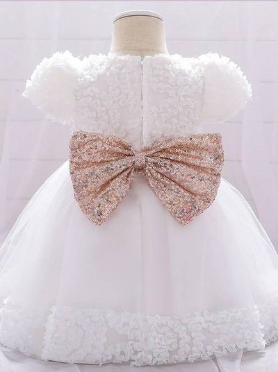 Baby dress has a floral bodice, a tulle skirt with floral hem, and a gold sequin belt with bow at the front and back