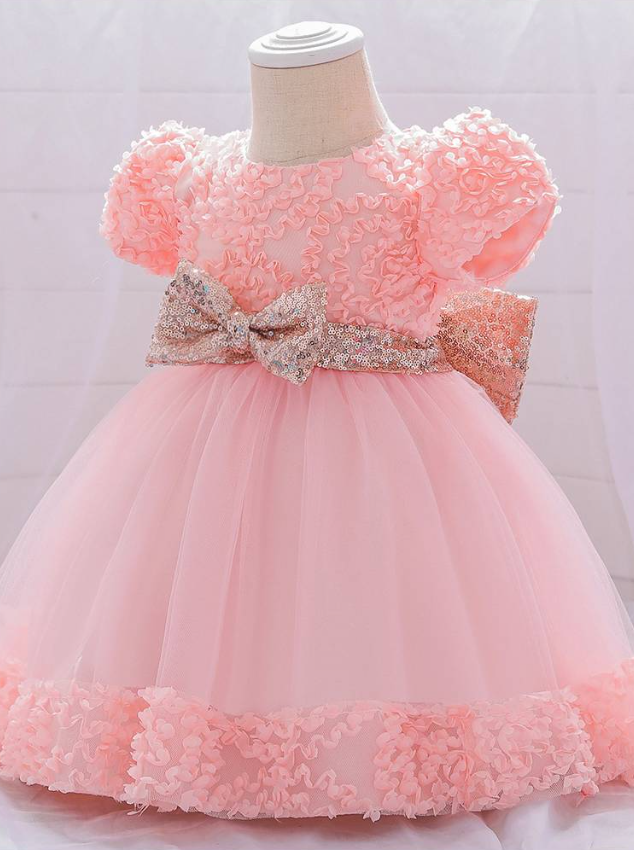 Baby dress has a floral bodice, a tulle skirt with floral hem, and a gold sequin belt with bow at the front and back