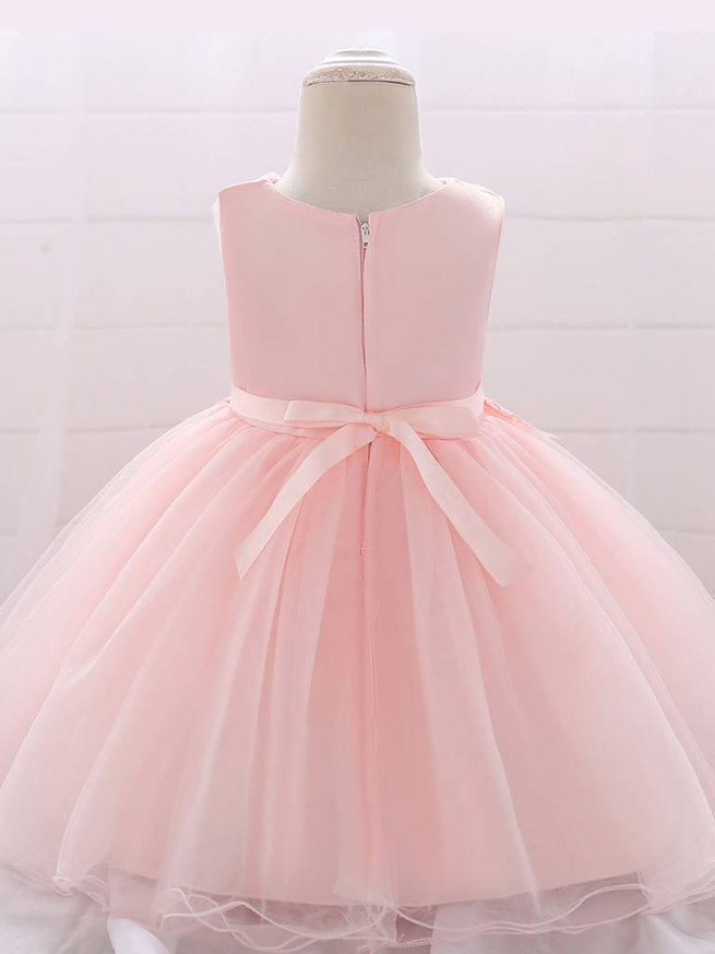 Baby dress has a tulle overlay with flower applique and a satin belt with rhinestone detail-pink