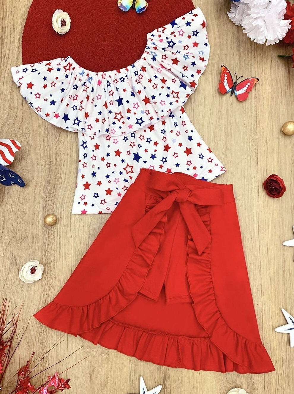 Girls three piece set features a white ruffle top with red and blue star print and red shorts with matching overlay wrap ruffle skirt